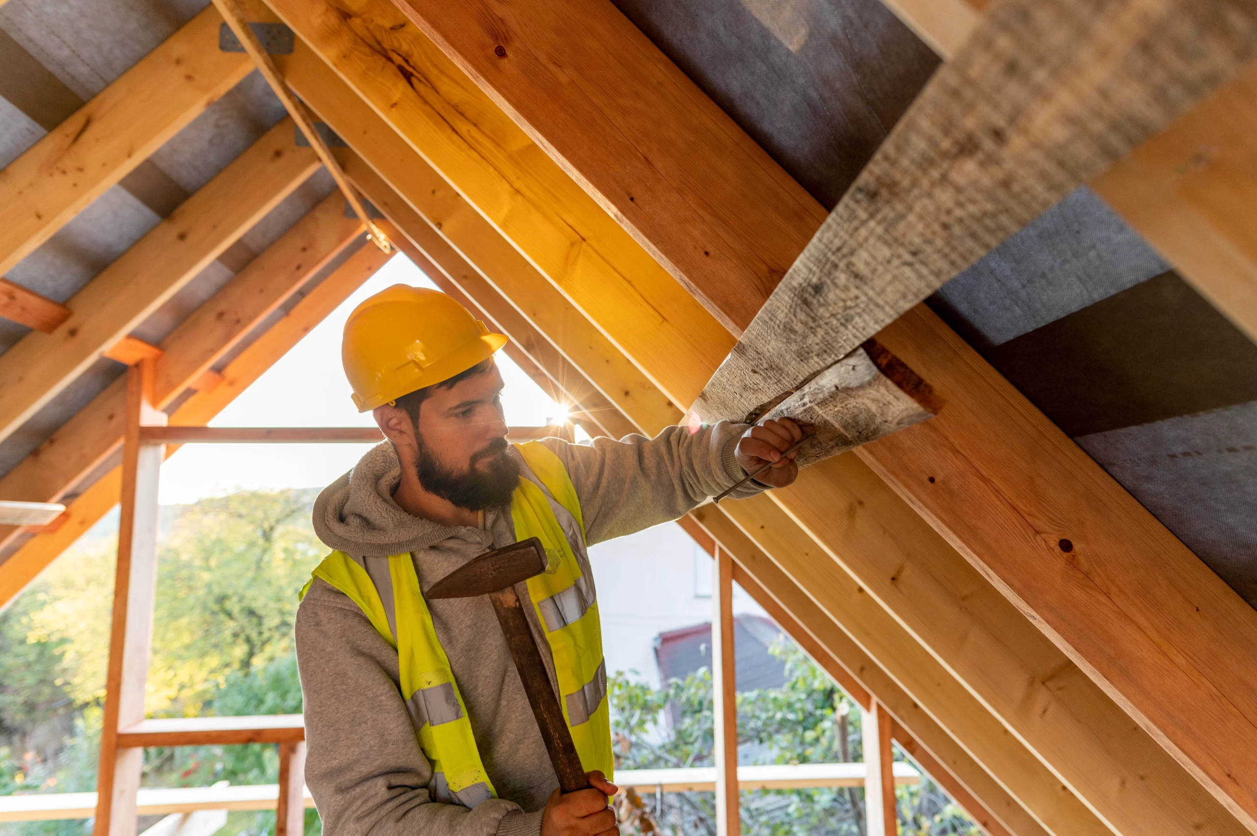 Bearded builder in safety gear hammering wooden slats during a roofing installation