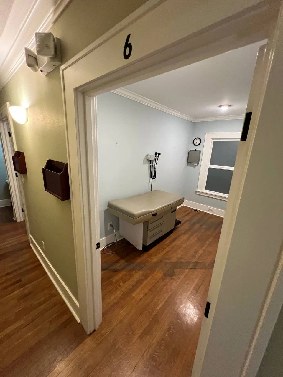 Examination room six with original wood flooring and medical table seen before the scheduled renovation project.