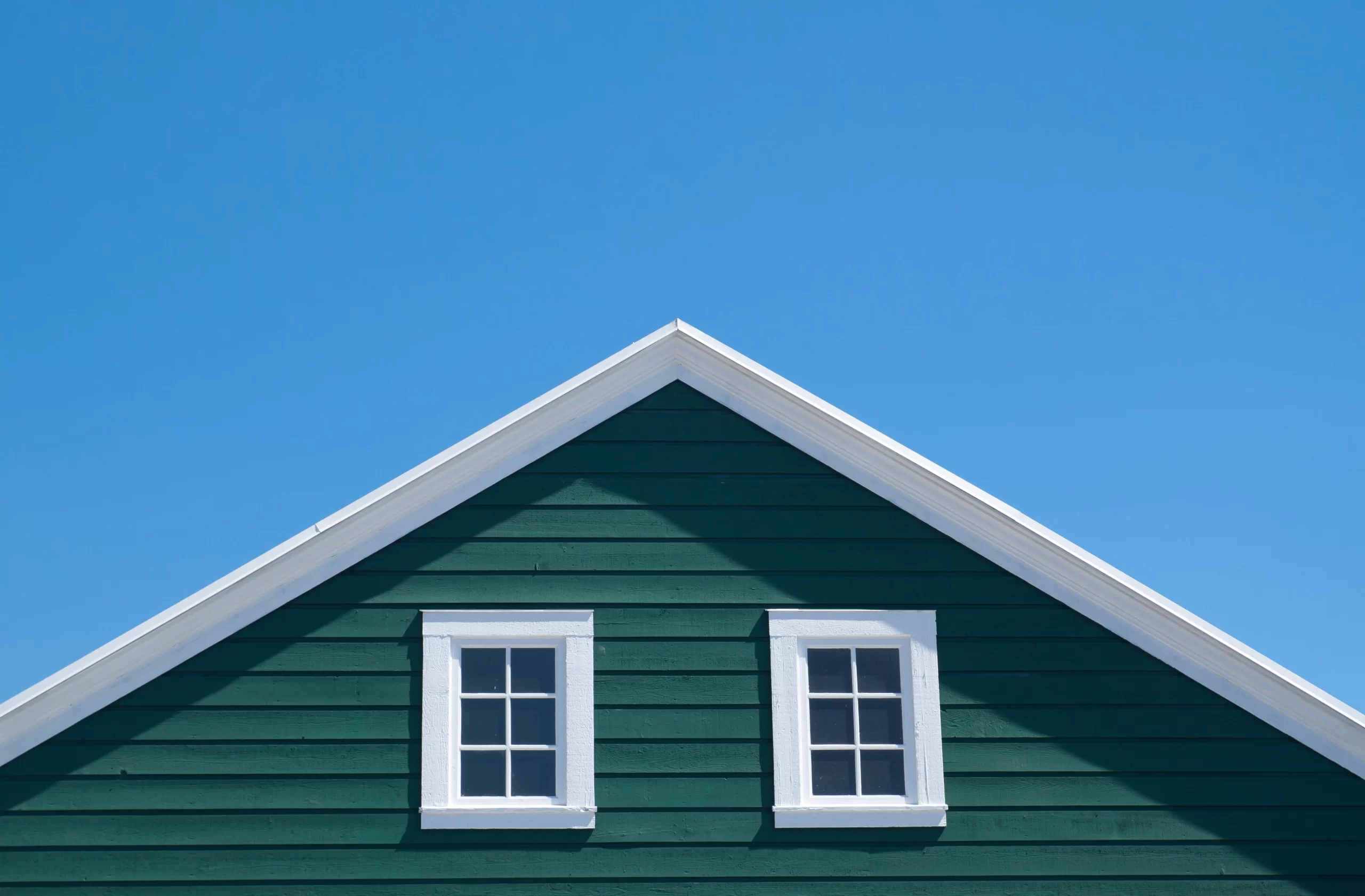 Dark green horizontal siding on a house gable with two white windows against a blue sky