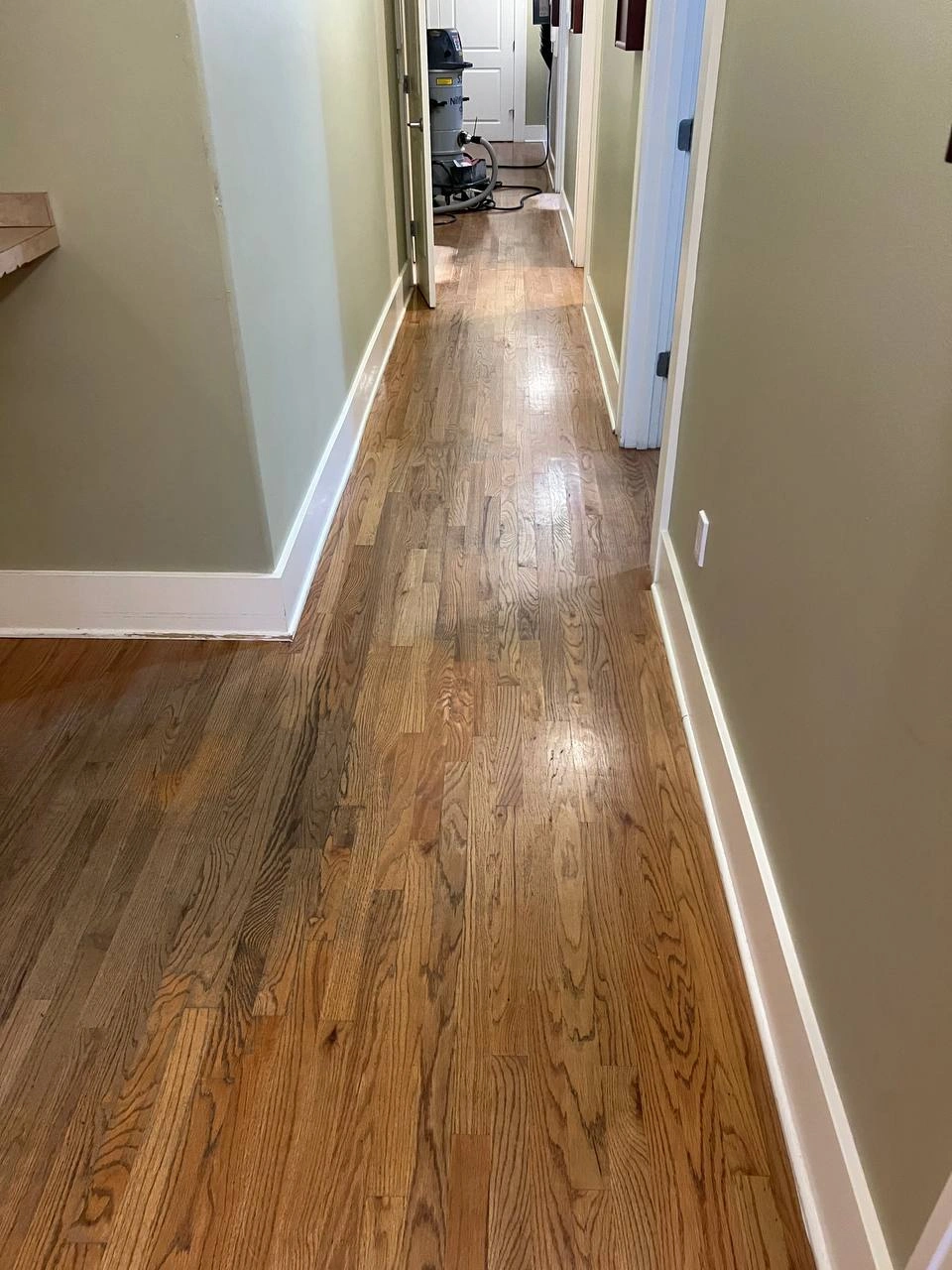 Worn oak flooring in a narrow hallway showing visible scuffs and aged finish before any restoration work begins.
