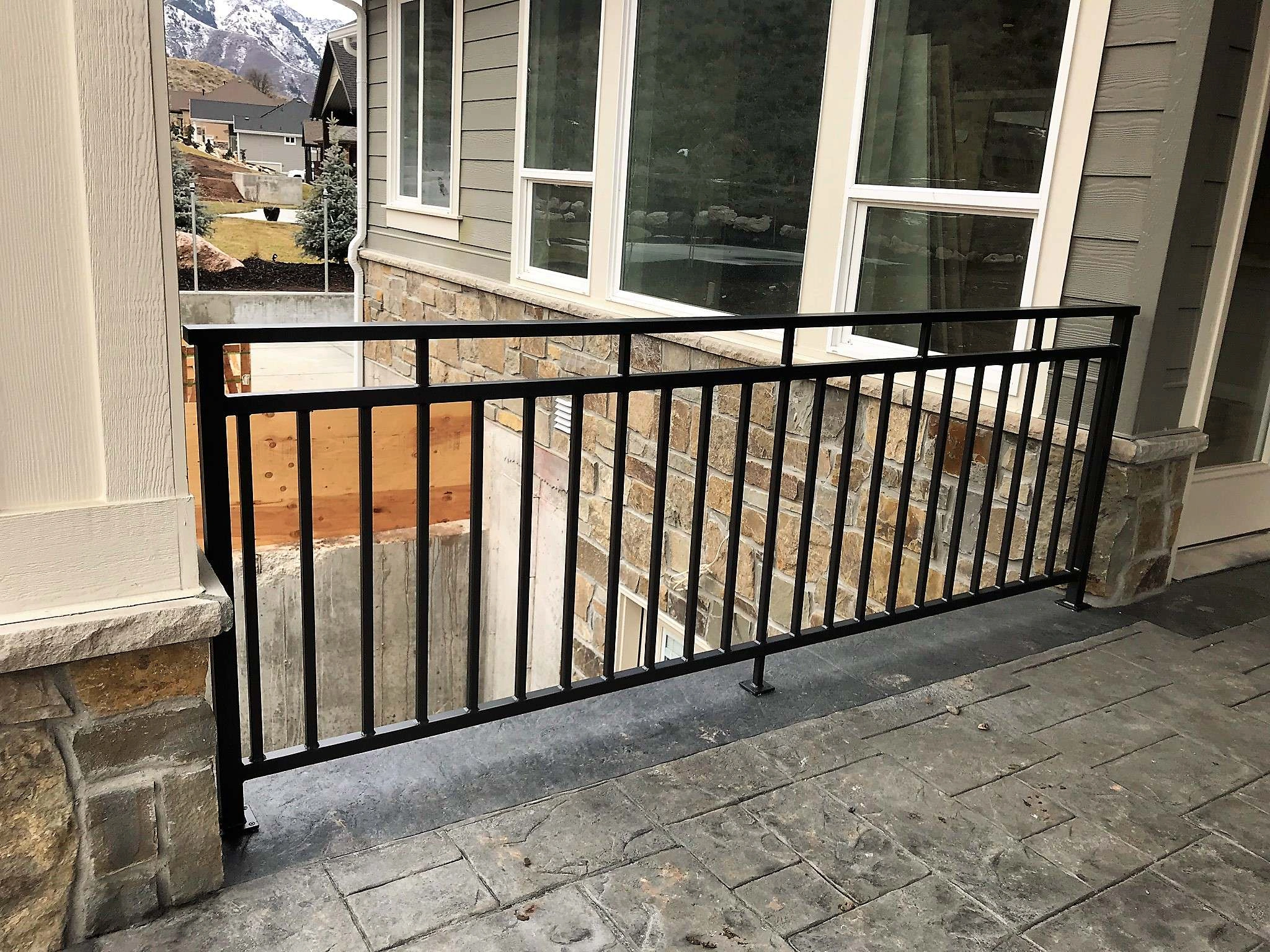 Black vertical Metal Rails installed on a stone-faced balcony overlooking a mountain neighborhood.
