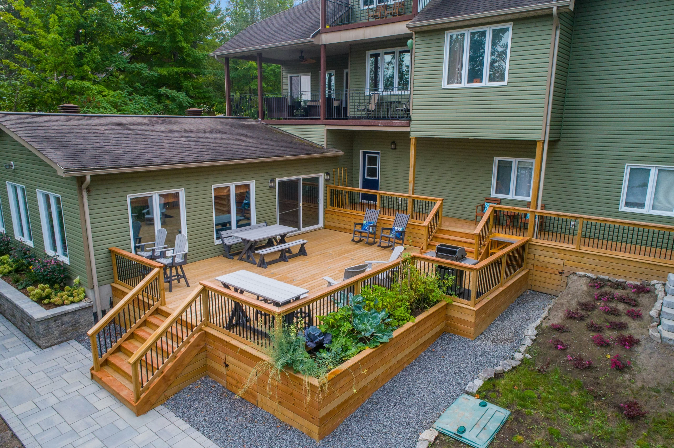 A large wooden patio featuring multiple Decks with gray outdoor furniture, integrated planters, and black railings.
