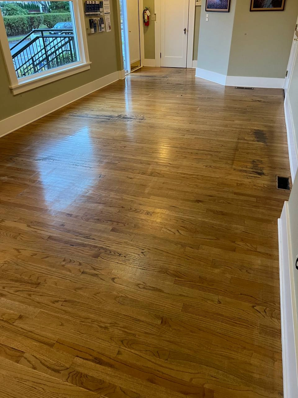 Spacious lobby area with glossy but worn hardwood flooring showing dark traffic marks before restoration.