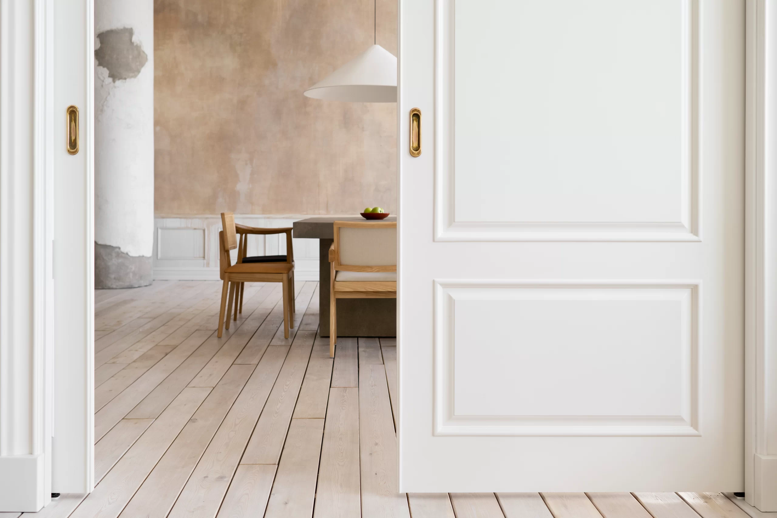 Large white sliding Doors with gold recessed handles open to reveal a modern dining area with wooden floors.