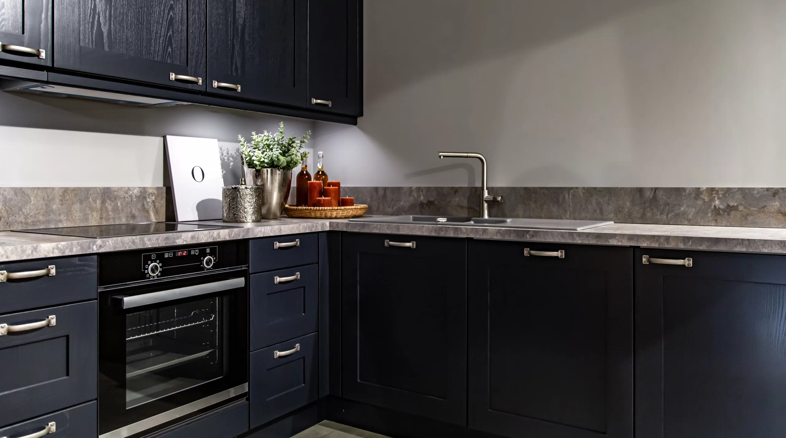 Dark navy shaker cabinets paired with grey stone Countertops and a matching backsplash in a modern kitchen.