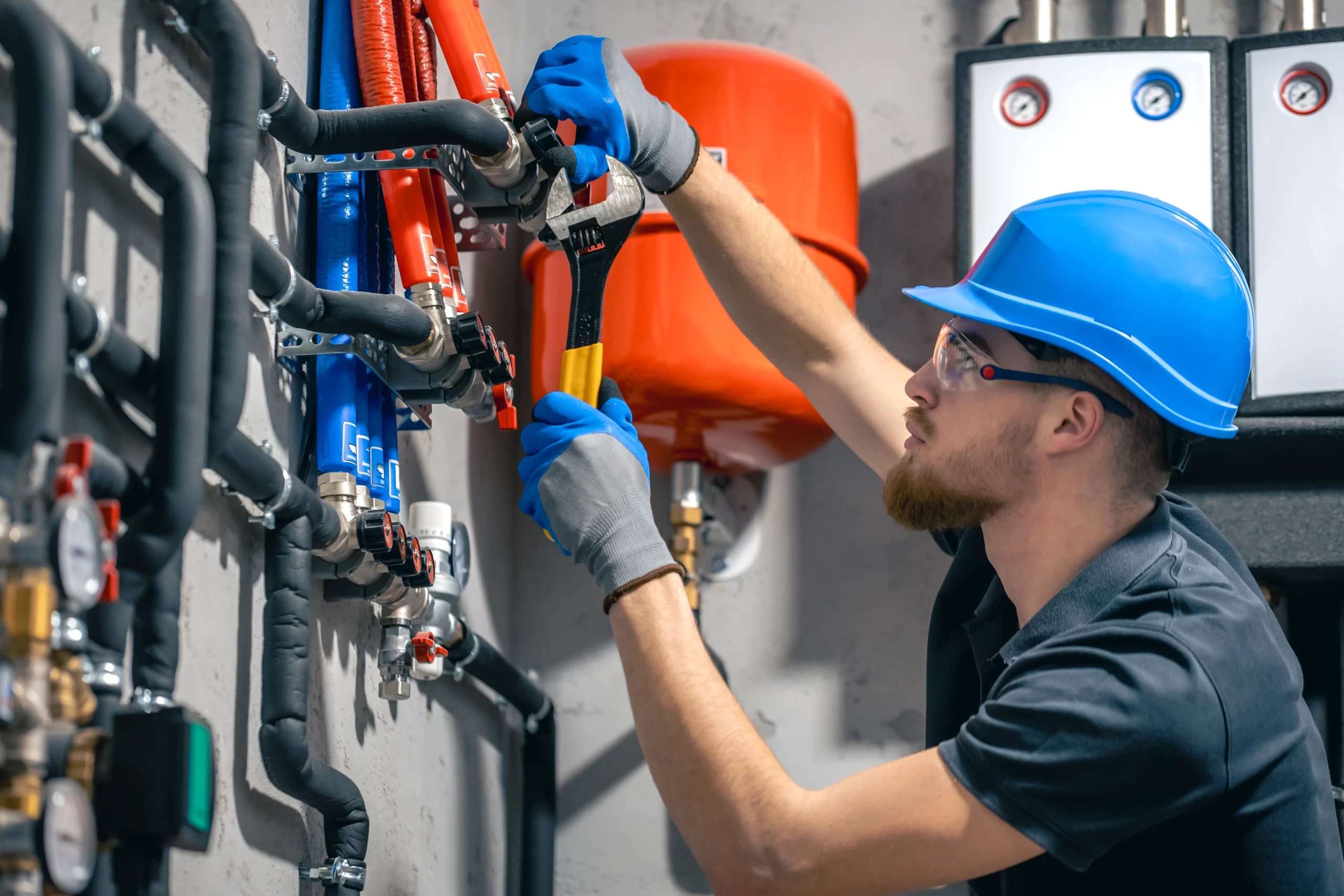 A worker in a hard hat uses a wrench to adjust insulated pipes during a residential Plumbing system check.