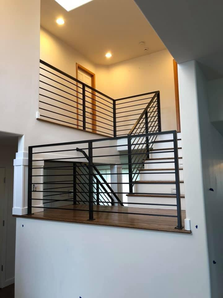 A multi-level interior featuring wooden landings and staircases protected by horizontal black Metal Rails.