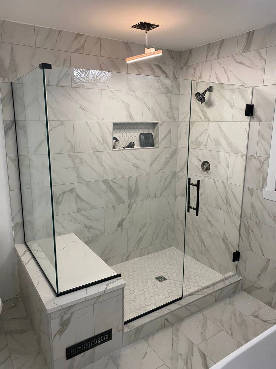 Modern marble shower with black hardware and clear Shower Glass Doors featuring a built-in bench.