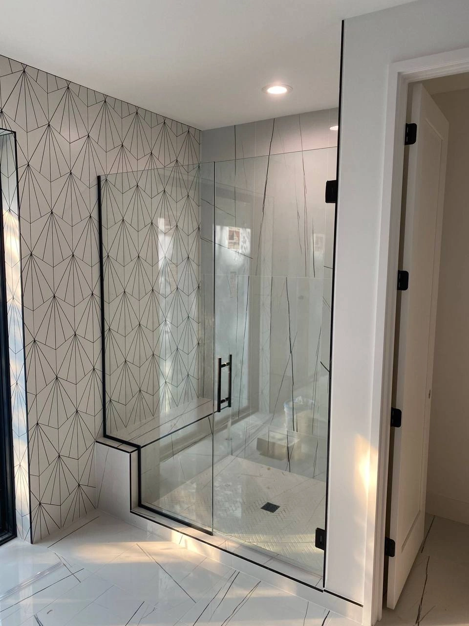 Clear Shower Glass Doors with matte black hardware installed against a striking geometric tile wall.