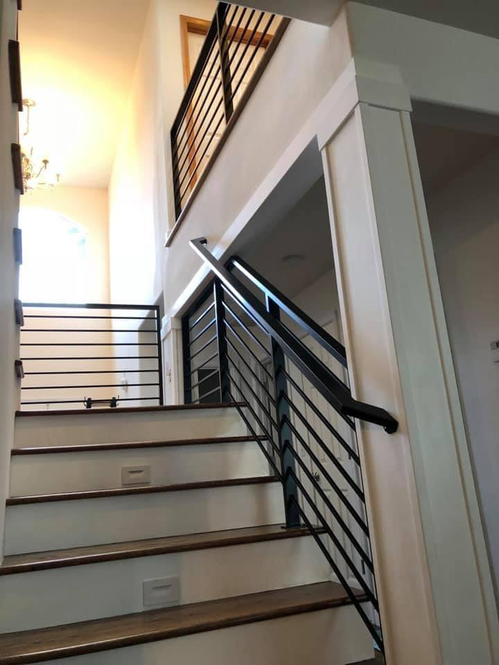 Modern wooden staircase featuring horizontal black Metal Rails and integrated step lighting in a bright home interior.
