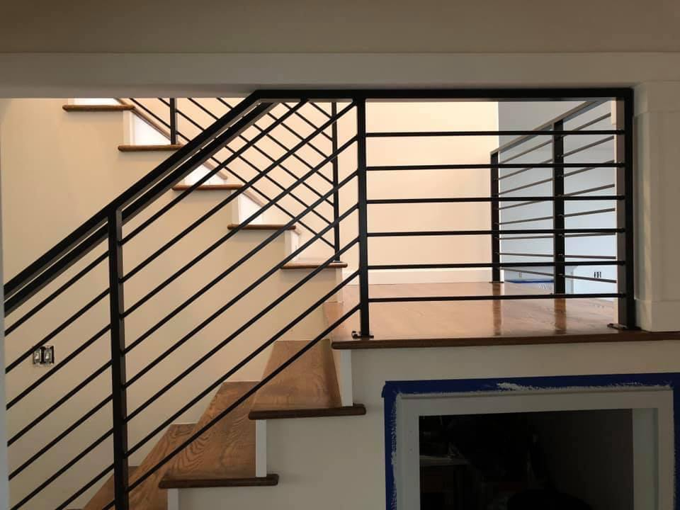 Close-up of a wooden staircase and landing featuring black horizontal Metal Rails in a bright, modern interior.