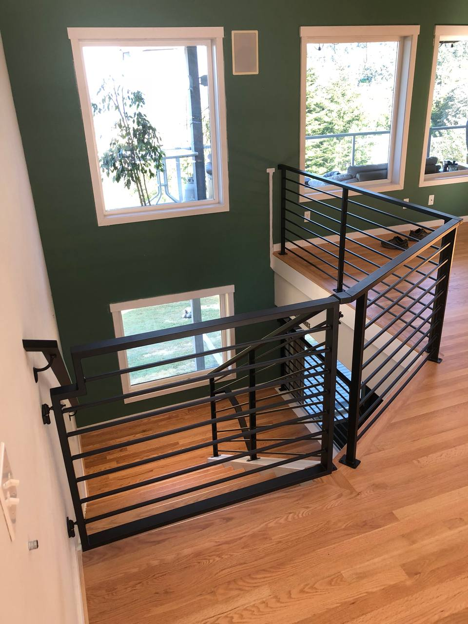 Top view of light wood flooring and a staircase accented by black horizontal Metal Rails against a green accent wall.