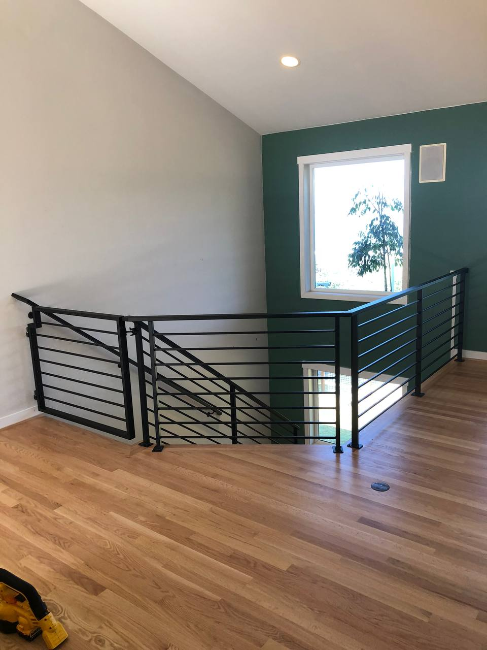 Top view of a wooden floor landing with horizontal black Metal Rails overlooking a staircase and green wall.