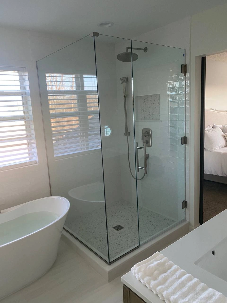 A view of a master bathroom featuring large Shower Glass Doors and a standalone bathtub.