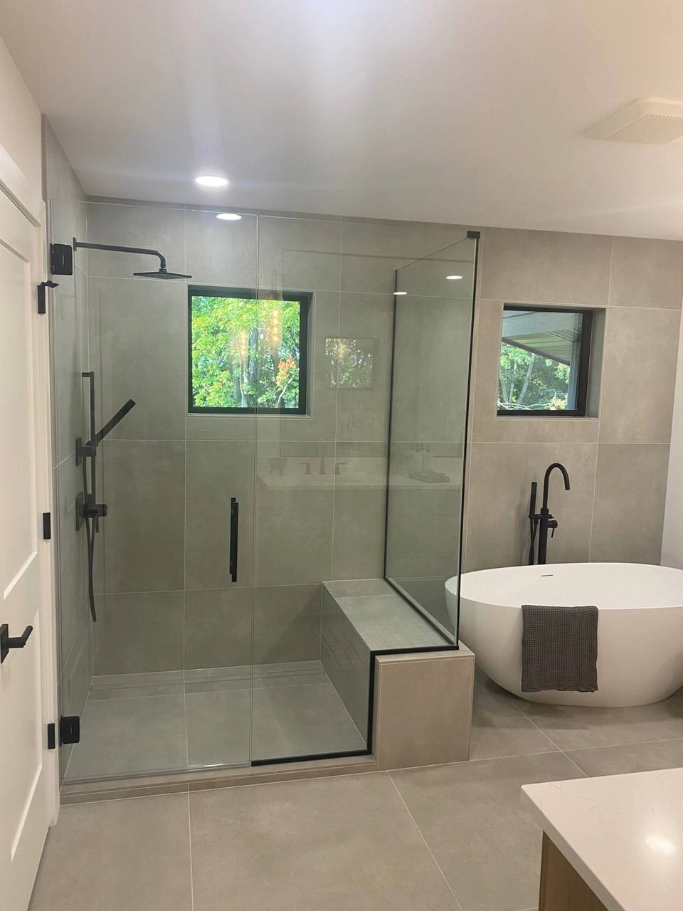 Large walk-in shower with sleek Shower Glass Doors and a built-in bench next to a standalone tub.