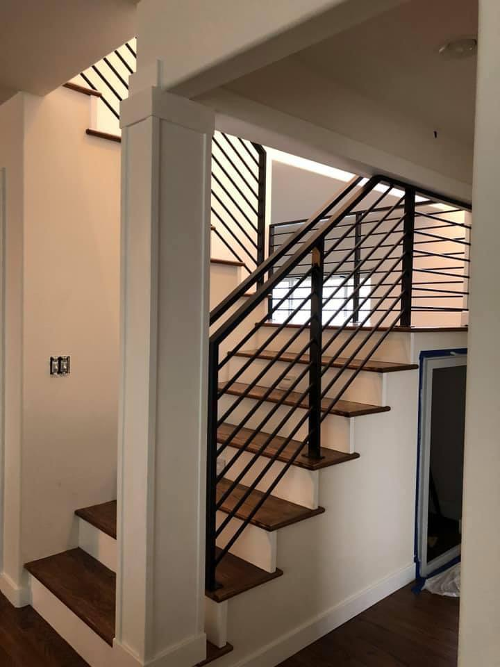 Wooden stairs with white risers and minimalist black Metal Rails installed in a bright modern house interior.