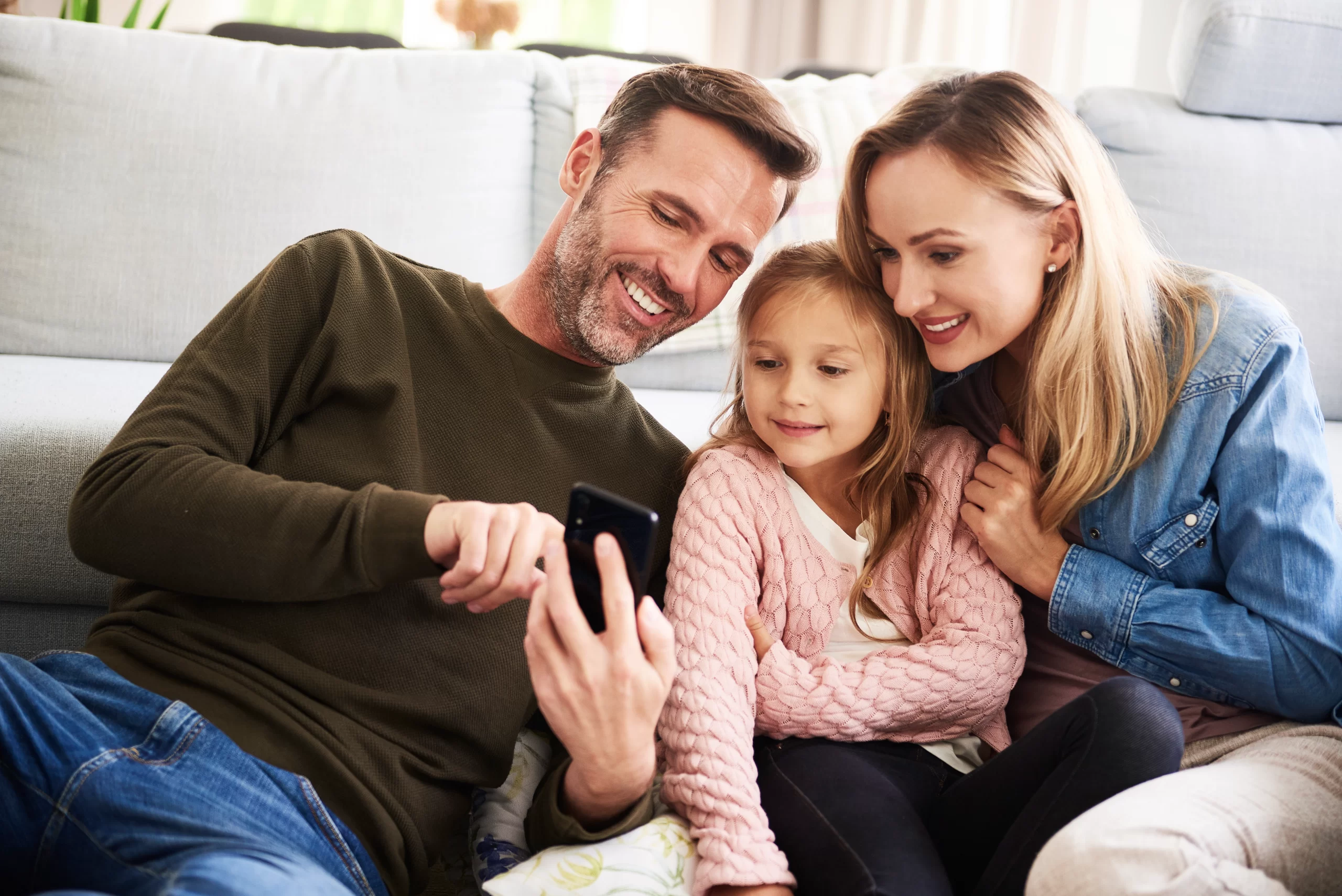 Family of three on a sofa, happily reviewing their approved home renovation financing plan on a holographic screen.