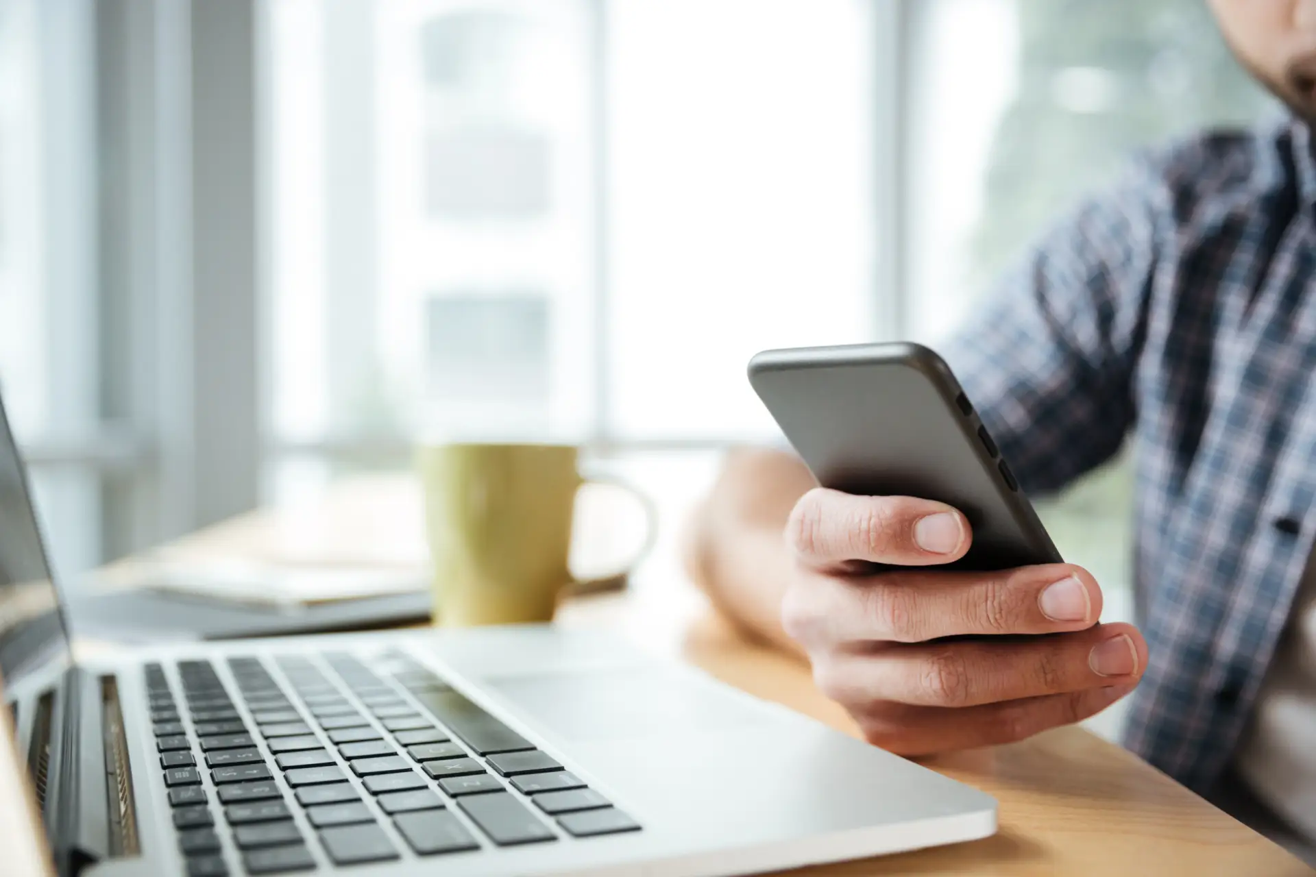 Close-up of a man holding a smartphone next to an open laptop while checking home renovation financing terms.